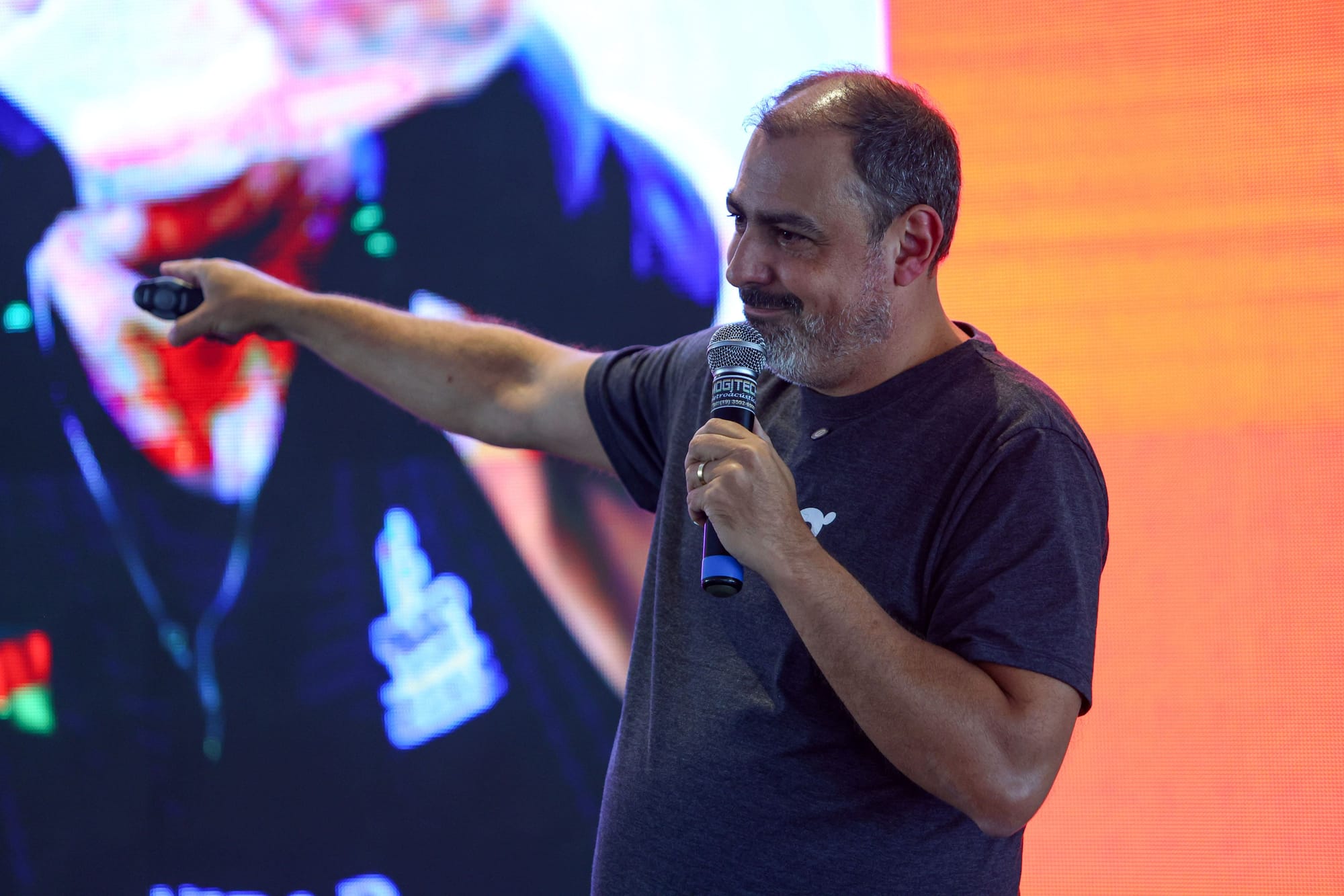 Homem com microfone e controle remoto aponta para o telão durante palestra na Run Expo 2025.