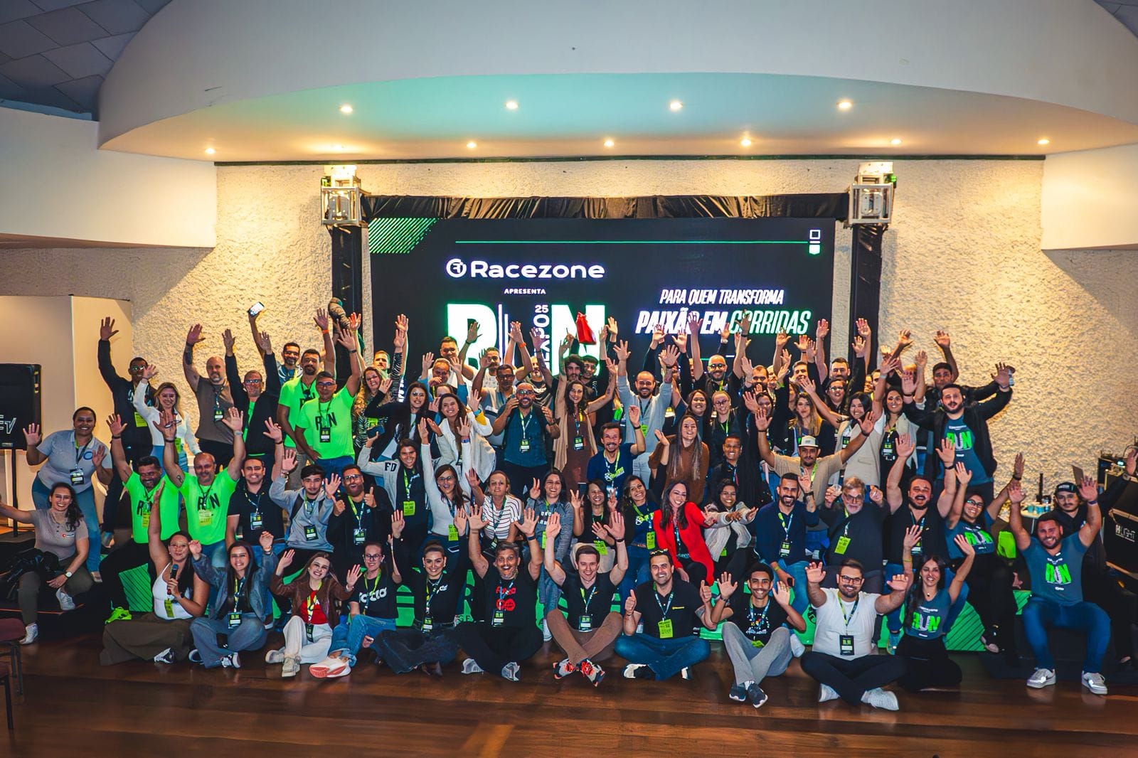 Participantes da Run Expo 2025 posa sorrindo com braço erguidos em frente ao palco.