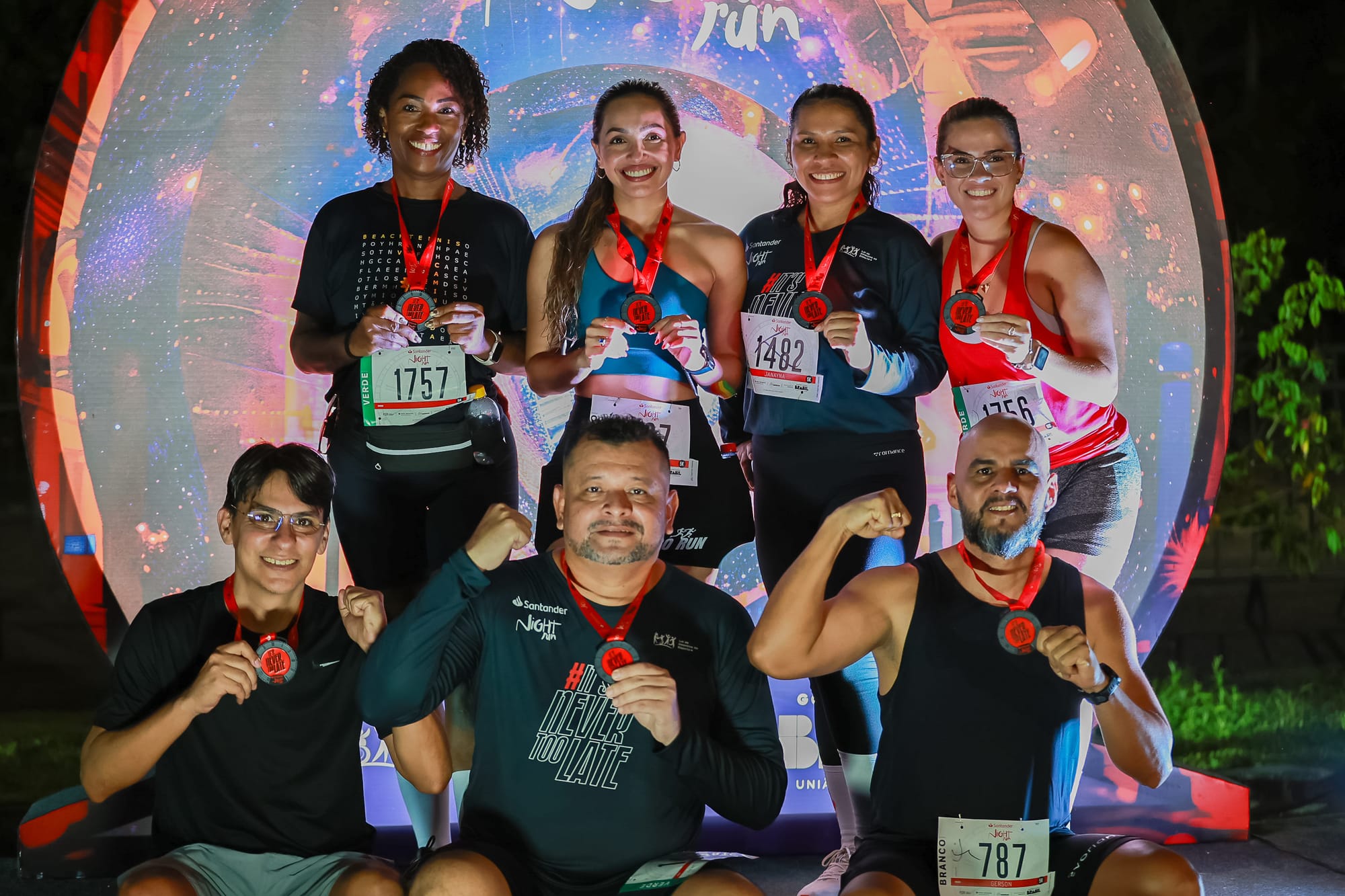 Grupo de sete corredores posa sorridente após a Night Run, exibindo suas medalhas de participação com orgulho. 